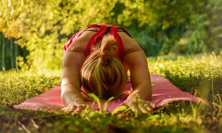 Frau macht Yoga auf einer Matte draußen im Grünen
